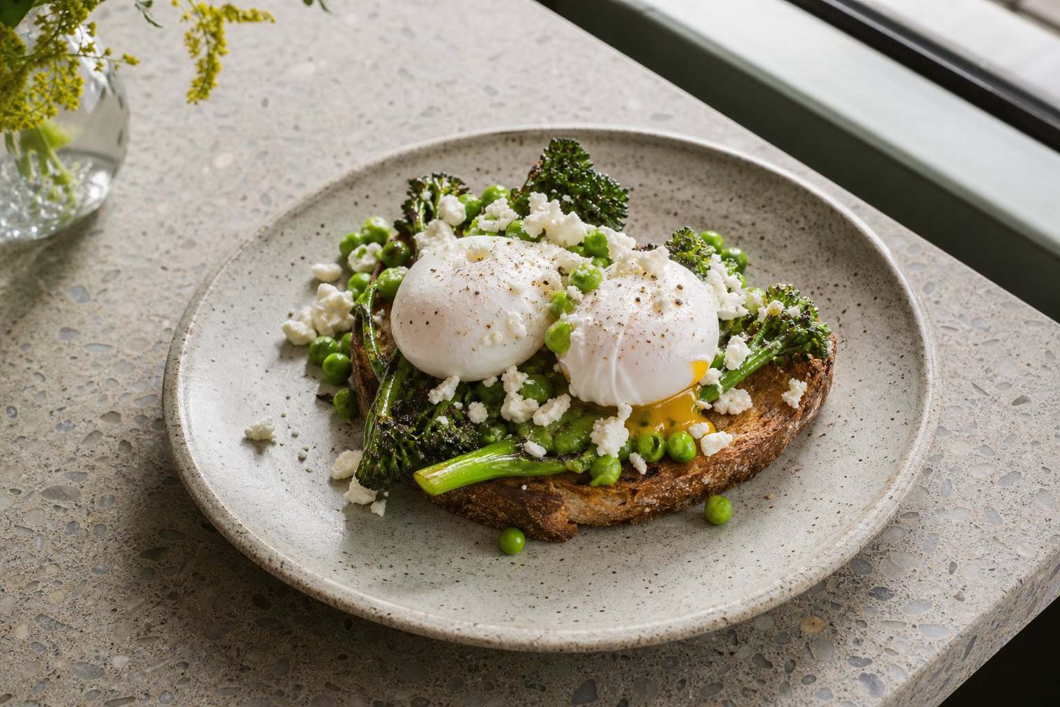 Poached eggs on sourdough with greens on a stoneware plate, by a window