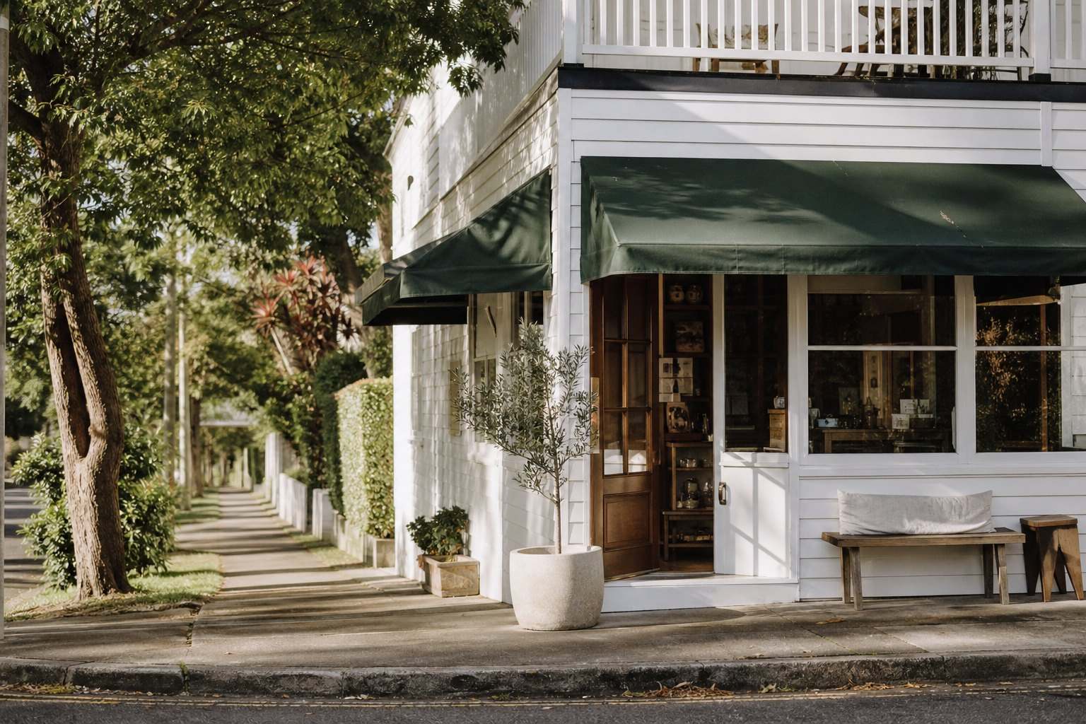 The shopfront of the cafe on a leafy lane, timber door open, a bench out the front